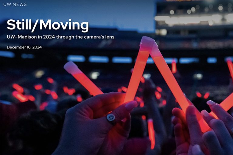 Screen shot of the hero area of a web story with the title "Still/Moving" over an image of hands holding up glow sticks in the shape of a "W"